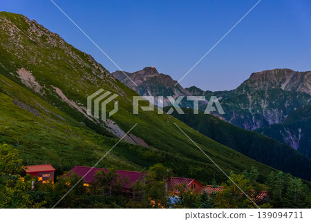 View from Jōnen Hut in the Northern Alps before dawn: Mount Kita-Hotaka and the lights of the mountain hut illuminated by the rising sun. View from Jōnen Hut in the Northern Alps before dawn: Mount Kita-Hotaka and the lights of the mountain hut illuminated by the rising sun. 139094711