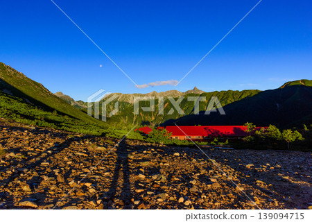The Northern Alps: Shadows stretching in the morning sun and the Yari-Hotaka mountain range; the lingering moon of dawn at Jōnen-Norikoshi on a clear morning. The Northern Alps: Shadows stretching in the morning sun and the Yari-Hotaka mountain range; the lingering moon of dawn at Jōnen-Norikoshi on a clear morning. 139094715