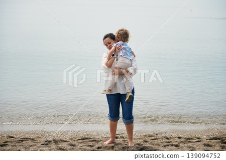 Mother Holding Child at Calm Beach Shore Embracing Tender Family Moment 139094752