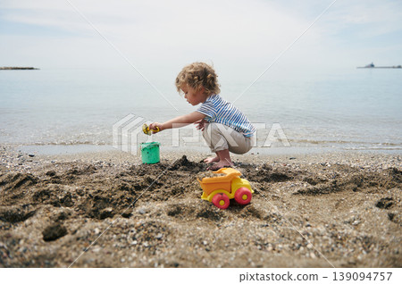 Young Child Playing With Bucket and Toy Truck on Sandy Beach by Calm Sea Young Child Playing With Bucket and Toy Truck on Sandy Beach by Calm Sea 139094757
