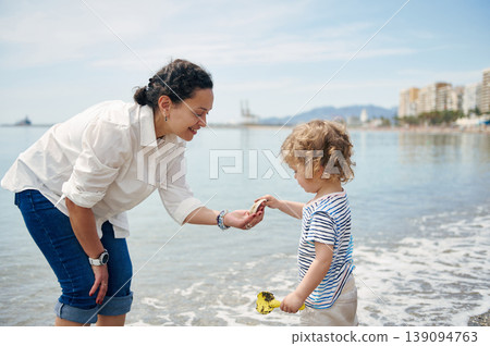 Mother and Toddler Playing on Sunny Urban Beach Sharing Seashells Mother and Toddler Playing on Sunny Urban Beach Sharing Seashells 139094763