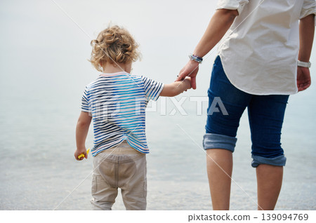 Mother Holding Hands With Young Child During Calm Seaside Beach Walk 139094769