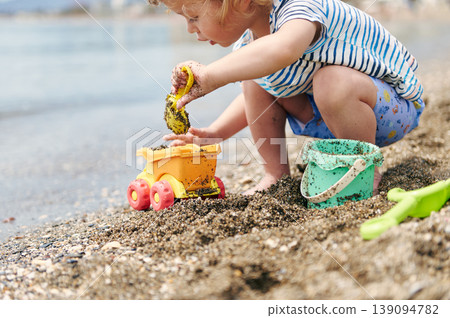 Toddler Playing With Sand Toys On A Sunny Beach Near The Water 139094782