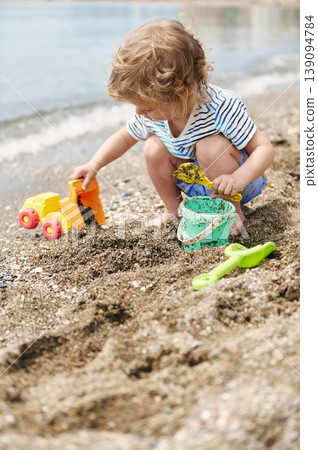 Toddler Playing With Toy Truck And Bucket On A Pebble Beach Shore Toddler Playing With Toy Truck And Bucket On A Pebble Beach Shore 139094784