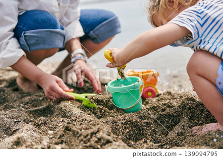 Child and Parent Playing With Bucket and Shovel on Sandy Beach Child and Parent Playing With Bucket and Shovel on Sandy Beach 139094795