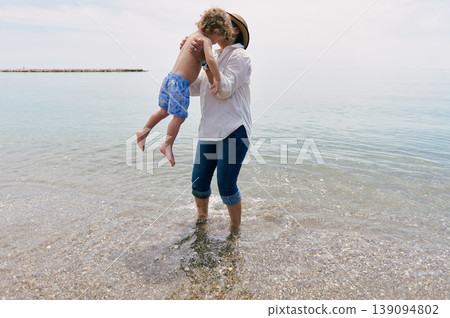 Mother Lifting And Kissing Young Son While Standing In Shallow Sea At Sunny Beach Mother Lifting And Kissing Young Son While Standing In Shallow Sea At Sunny Beach 139094802