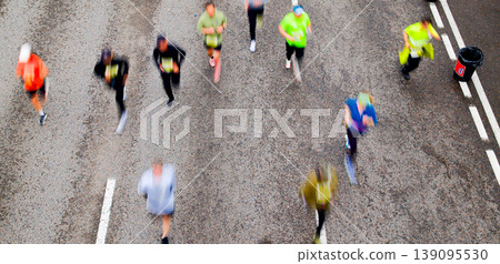 Aerial overhead view of crowd of runners with motion blur competing in urban city marathon race event Aerial overhead view of crowd of runners with motion blur competing in urban city marathon race event 139095530