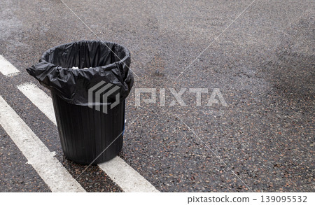 Black plastic garbage trash bin bag on gray asphalt road surface with white line marking outdoors 139095532