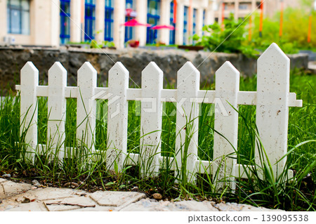 Classic white wooden picket fence with green grass and bushes in residential neighborhood Classic white wooden picket fence with green grass and bushes in residential neighborhood 139095538
