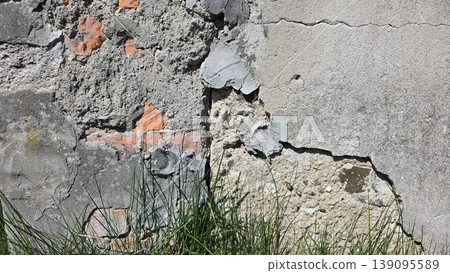 Close-up of weathered old wall with peeling plaster and exposed red bricks near green grass. Concept of urban decay, time, and history Close-up of weathered old wall with peeling plaster and exposed red bricks near green grass. Concept of urban decay, time, and history 139095589