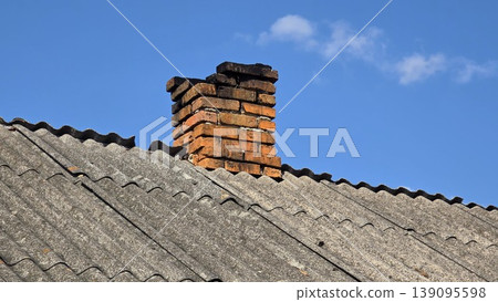 Old red brick chimney on weathered slate roof against clear blue sky with white clouds, concept of traditional architecture and rural house heating Old red brick chimney on weathered slate roof against clear blue sky with white clouds, concept of traditional architecture and rural house heating 139095598