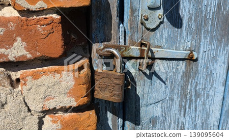 Old blue wooden door with rusty padlock and brick wall detail, weathered architectural background for security, abandonment, vintage and urban themes. 139095604