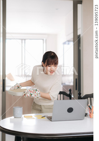 Happy asian woman working from home using modern laptop technology while studying online for business and simultaneously managing household laundry chores smiling brightly with joyful expression Happy asian woman working from home using modern laptop technology while studying online for business and simultaneously managing household laundry chores smiling brightly with joyful expression 139095723