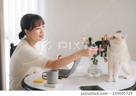 Smiling asian woman working online studying business technology at home feeding cat Smiling asian woman working online studying business technology at home feeding cat 139095727