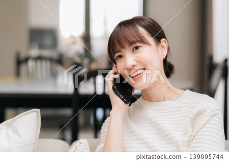 Cheerful asian woman smiling happily at home talking on smartphone while working online for modern business using digital technology and studying new effective communication skills carefully Cheerful asian woman smiling happily at home talking on smartphone while working online for modern business using digital technology and studying new effective communication skills carefully 139095744