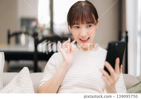 Happy asian woman sitting at home working on business and studying online using modern technology while smiling cheerfully during video call on mobile phone Happy asian woman sitting at home working on business and studying online using modern technology while smiling cheerfully during video call on mobile phone 139095750