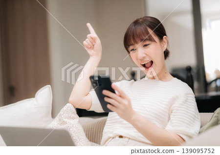 Excited young asian woman sits comfortably at home working and studying online using modern mobile technology for business feeling thrilled looking at smart phone screen pointing finger up Excited young asian woman sits comfortably at home working and studying online using modern mobile technology for business feeling thrilled looking at smart phone screen pointing finger up 139095752