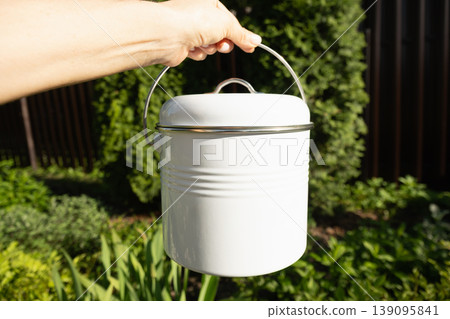 White compost bin with lid held outdoors in garden White compost bin with lid held outdoors in garden 139095841