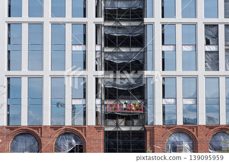 Builders on a suspended platform working on a modern glass building facade Builders on a suspended platform working on a modern glass building facade 139095959
