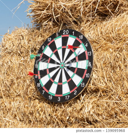 A dartboard on a haystack with several darts hitting and missing 139095968