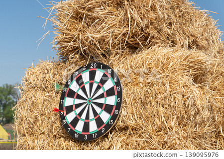 A dartboard on a haystack with a red dart missing the board 139095976
