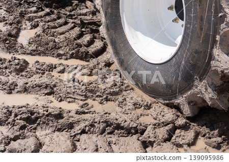 A heavy tractor wheel with deep treads in thick brown mud A heavy tractor wheel with deep treads in thick brown mud 139095986