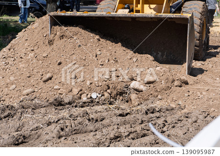 Front loader bucket filled with dirt and stones on a muddy construction site Front loader bucket filled with dirt and stones on a muddy construction site 139095987
