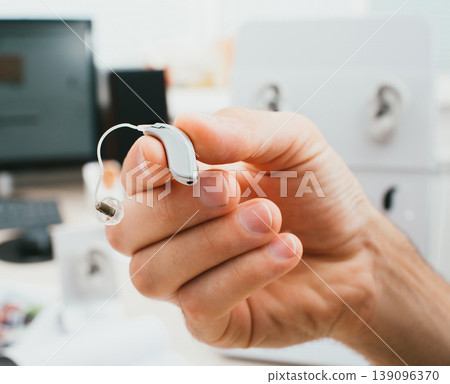 BTE hearing aid close-up in a male hand. Hearing solution, man holds a hearing aid, macro BTE hearing aid close-up in a male hand. Hearing solution, man holds a hearing aid, macro 139096370