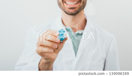 Positive audiologist holding in his hands molded individual hearing aid earmolds for his patient, close-up. Hearing solution 139096389