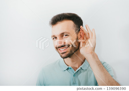 Check your hearing. Positive man holds his hand near his ear, on a gray background. Ear health, treatment and diagnosis of hearing Check your hearing. Positive man holds his hand near his ear, on a gray background. Ear health, treatment and diagnosis of hearing 139096390