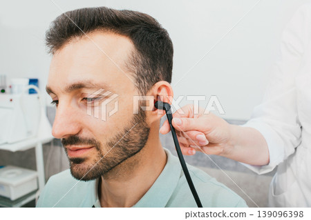 Diagnosis of hearing impairment, tympanometry, hearing test. A man during a hearing diagnostic procedure, and a special earphone in his ear. Diagnosis of hearing impairment, tympanometry, hearing test. A man during a hearing diagnostic procedure, and a special earphone in his ear. 139096398