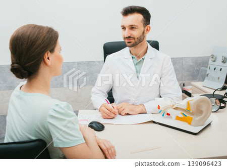 Young mixed race audiologist consults a woman patient in his office. Treatment of hearing loss in adults Young mixed race audiologist consults a woman patient in his office. Treatment of hearing loss in adults 139096423
