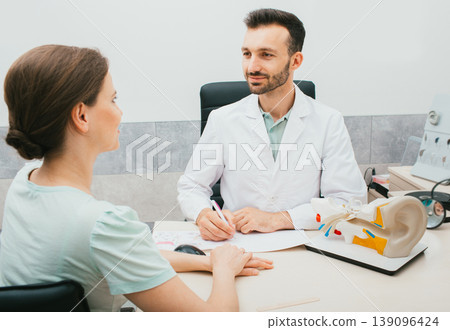 Young mixed race audiologist consults a woman patient in his office. Treatment of hearing loss in adults. Hearing clinic 139096424