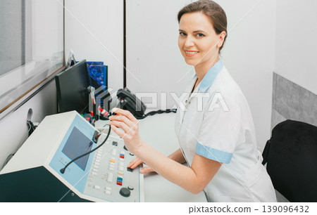 Positive audiologist doctor woman in her office at the hearing clinic during a patient hearing test in special audio room 139096432