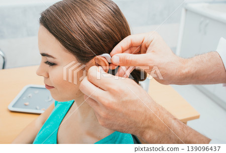 Audiologist inserting hearing aid on female ear, close-up . Deafness treatment, hearing solution Audiologist inserting hearing aid on female ear, close-up . Deafness treatment, hearing solution 139096437