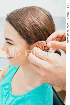 Audiologist inserting hearing aid on female ear, close-up . Deafness treatment, hearing solution 139096439