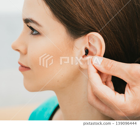 Young patient with Intra-ear hearing aid, close-up on female ear. The hearing solution, audiologist inserting hearing aid Young patient with Intra-ear hearing aid, close-up on female ear. The hearing solution, audiologist inserting hearing aid 139096444