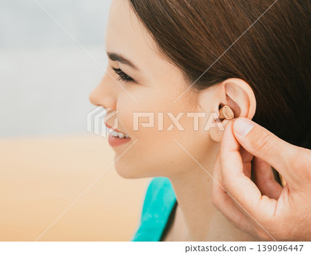 Young patient with Intra-ear hearing aid, close-up on female ear. The hearing solution, audiologist inserting hearing aid Young patient with Intra-ear hearing aid, close-up on female ear. The hearing solution, audiologist inserting hearing aid 139096447