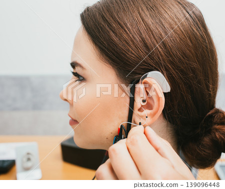 Audiologist programming hearing aid acoustic response using the software. Young woman getting hearing aid adjustments Audiologist programming hearing aid acoustic response using the software. Young woman getting hearing aid adjustments 139096448