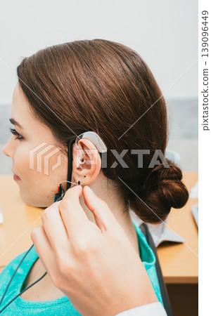 Audiologist programming hearing aid acoustic response using the software. Young woman getting hearing aid adjustments Audiologist programming hearing aid acoustic response using the software. Young woman getting hearing aid adjustments 139096449