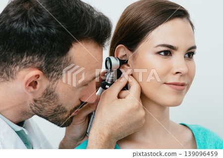 Hearing exam. Hispanic woman during a hearing test, an audiologist with an otoscope checking ear of adult patient, close-up 139096459