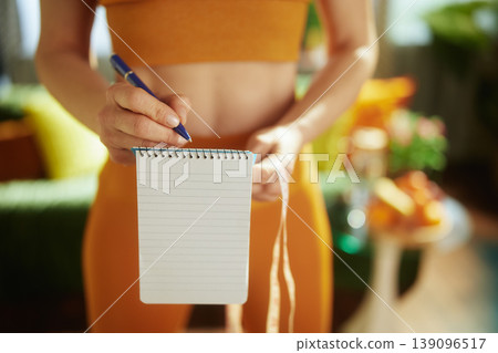 Woman Tracking Fitness Progress with Notebook and Measuring Tape Woman Tracking Fitness Progress with Notebook and Measuring Tape 139096517