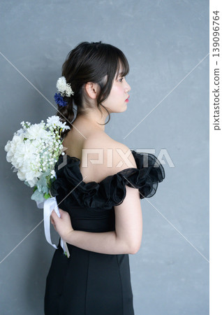 一位身穿黑色洋裝的日本女子手捧花束,背景為灰色。 一位身穿黑色洋裝的日本女子手捧花束,背景為灰色。 139096764