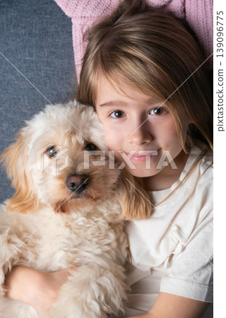 Portrait of a Little Girl Hugging Her Cream Maltipoo Puppy on a Couch 139096775