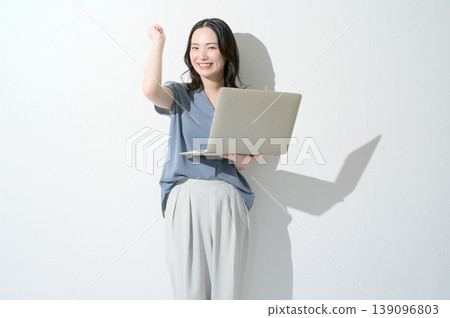 一位日本女性在白色背景下,手持筆記型電腦,做出勝利的手勢。 一位日本女性在白色背景下,手持筆記型電腦,做出勝利的手勢。 139096803