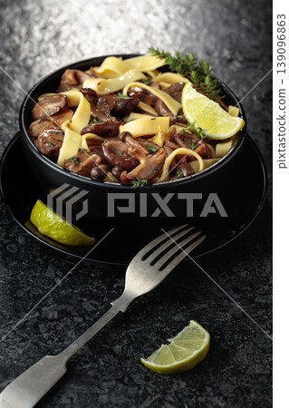 Shimeji and shiitake mushrooms stir-fried with soy sauce, garlic and thyme, served with noodles and lime slice in a black ceramic bowl. Shimeji and shiitake mushrooms stir-fried with soy sauce, garlic and thyme, served with noodles and lime slice in a black ceramic bowl. 139096863