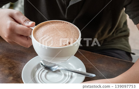 Closeup image of hands holding a cup of hot chocolate on rustic wooden background Closeup image of hands holding a cup of hot chocolate on rustic wooden background 139097753