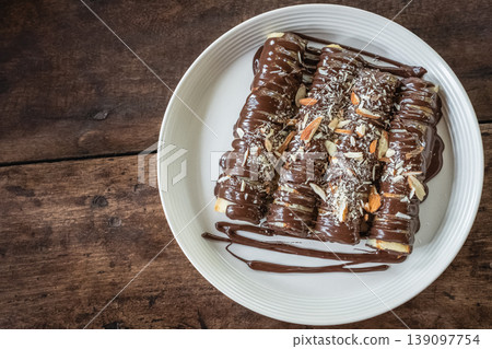 Delicious crepes with chocolate sauce and sprinkled with almonds on white plate on wooden background Delicious crepes with chocolate sauce and sprinkled with almonds on white plate on wooden background 139097754