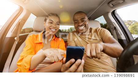 Young African American couple using smartphone together inside car Young African American couple using smartphone together inside car 139098691