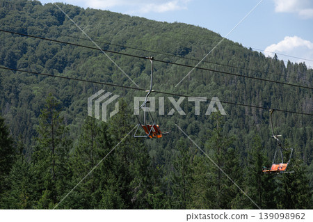 Empty chairlift ascending over a lush green mountain forest. 139098962
